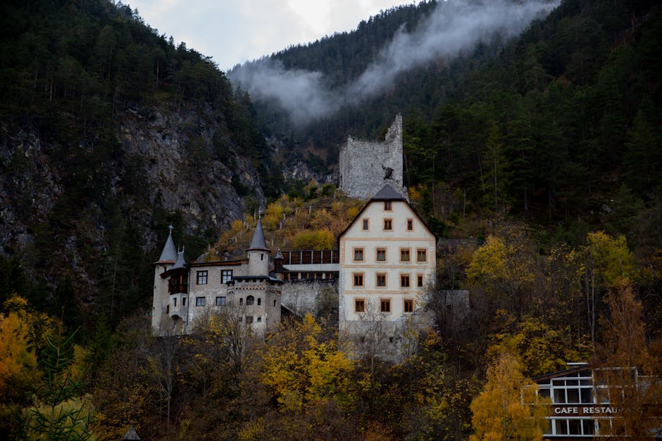 Enchanting castle nestled in Austrian forest during fall, surrounded by mountains and rich autumn foliage.