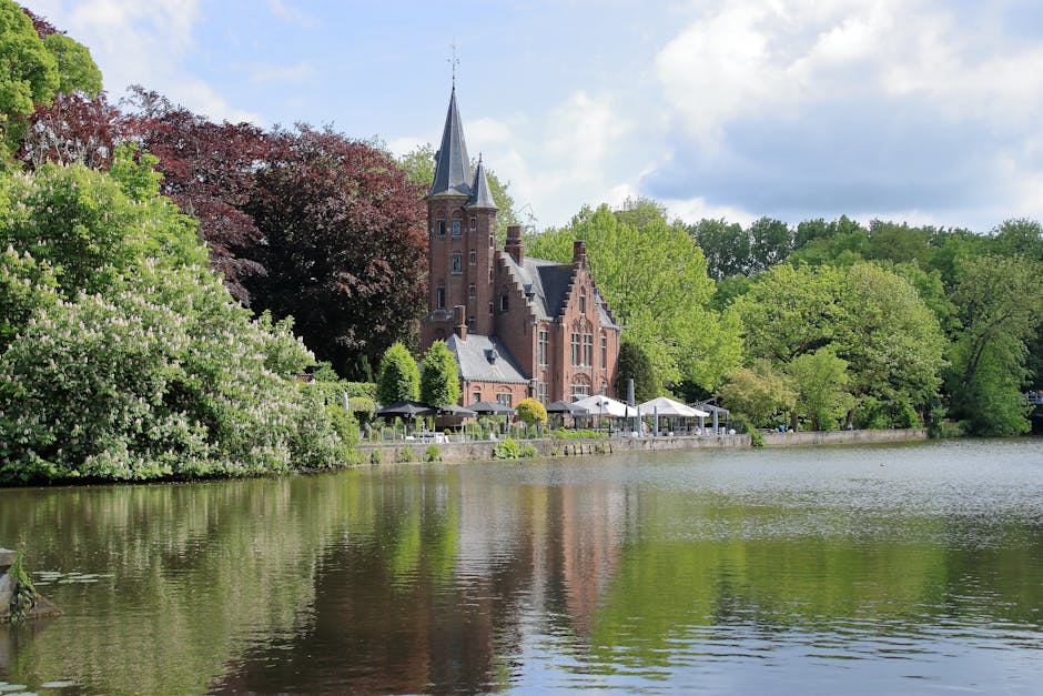 Beautiful European castle by the lake surrounded by lush greenery, reflecting peaceful charm.
